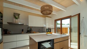 A modern kitchen with wooden cabinets, a central island, a built-in oven, and a hanging light fixture. - Villa 'Marloria' with Mountain Views, Wi-Fi, and Air Conditioning (Crestatx)