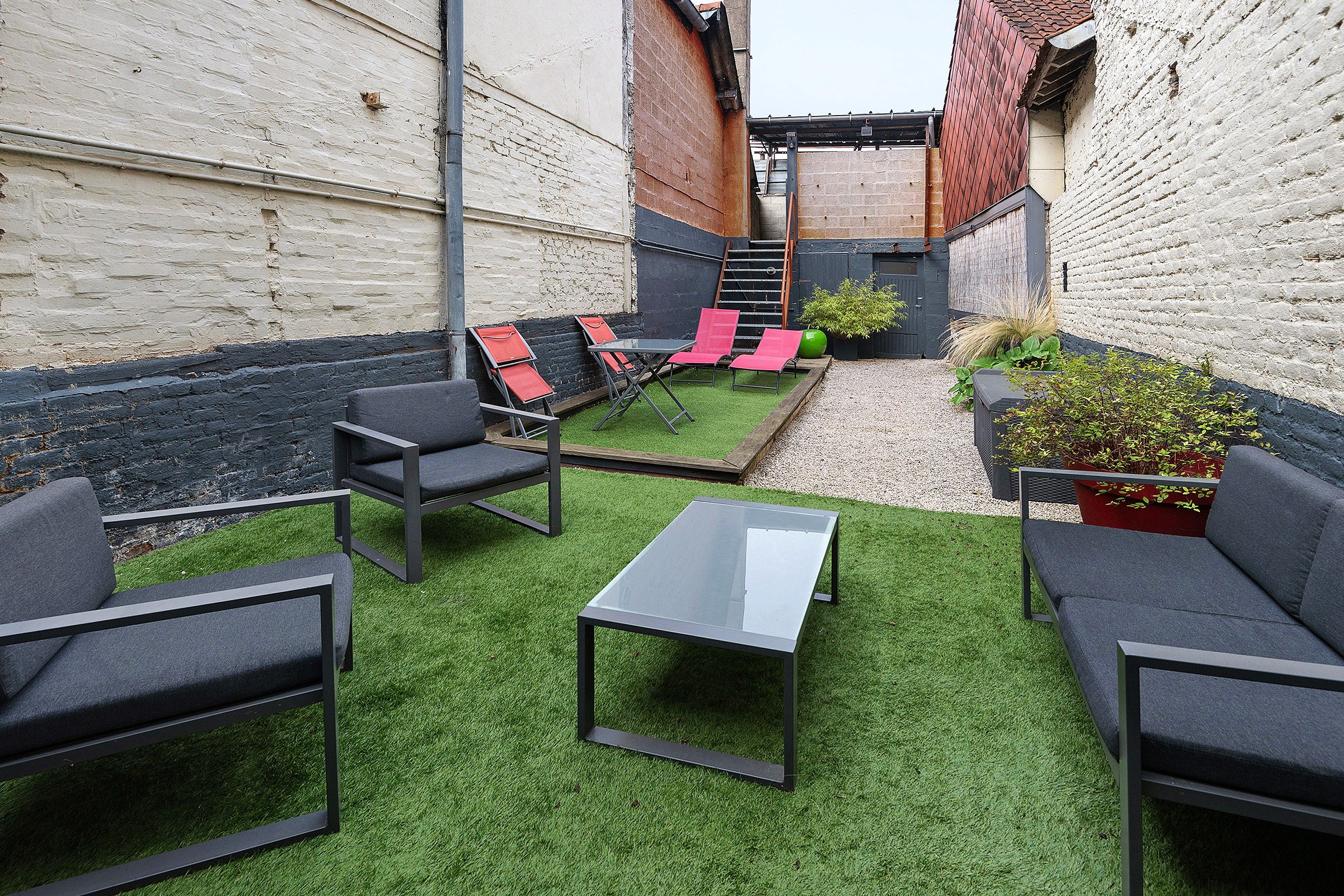 Un patio con césped artificial, mobiliario exterior y una escalera que lleva a un nivel superior.