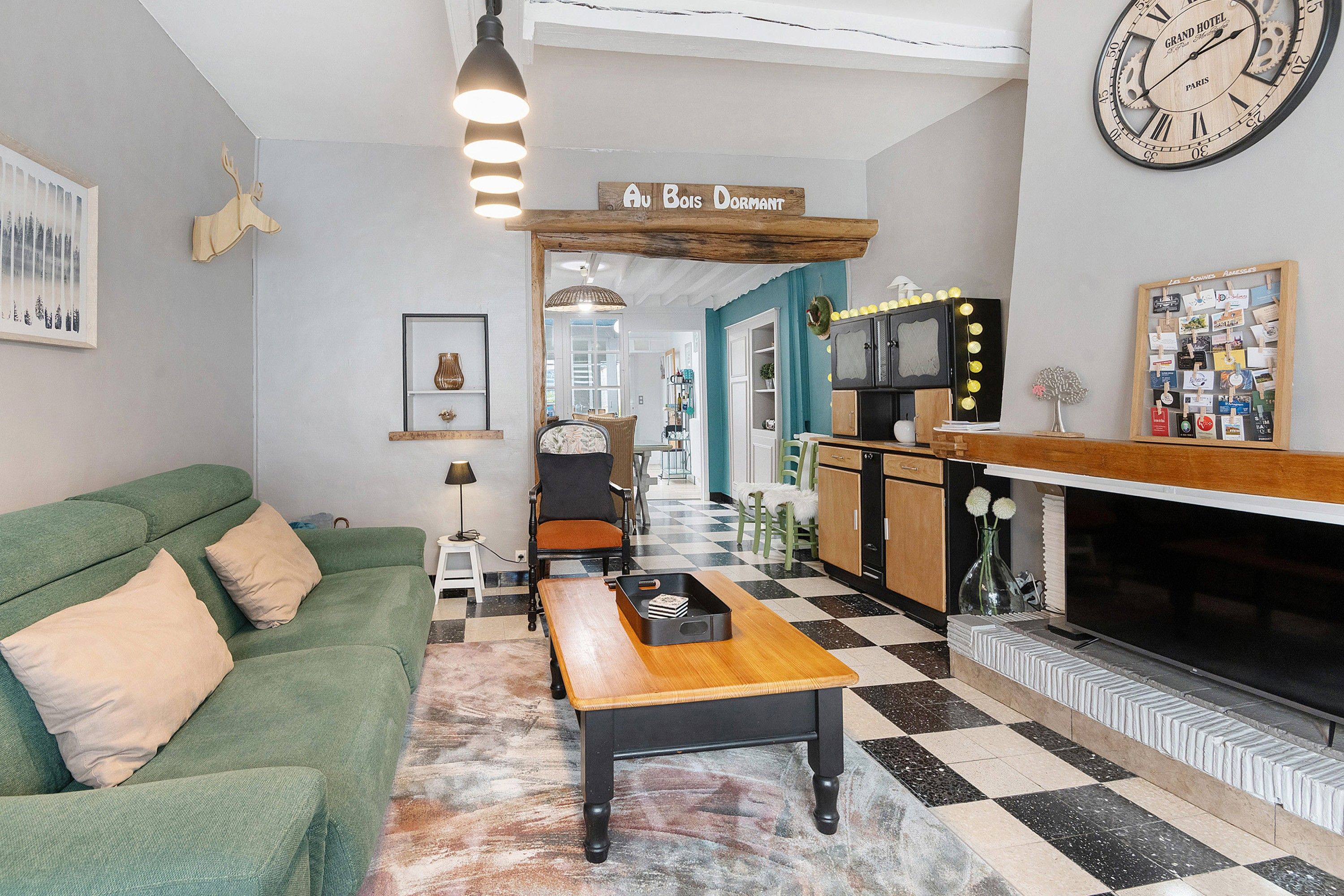 Une chambre d’hôtel avec un sol à carreaux, un canapé vert, une table en bois, une cheminée et une horloge murale.