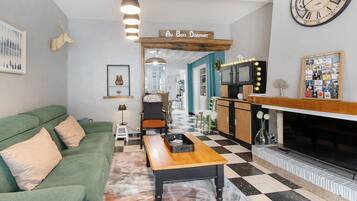 Une chambre d’hôtel avec un sol à carreaux, un canapé vert, une table en bois, une cheminée et une horloge murale.
