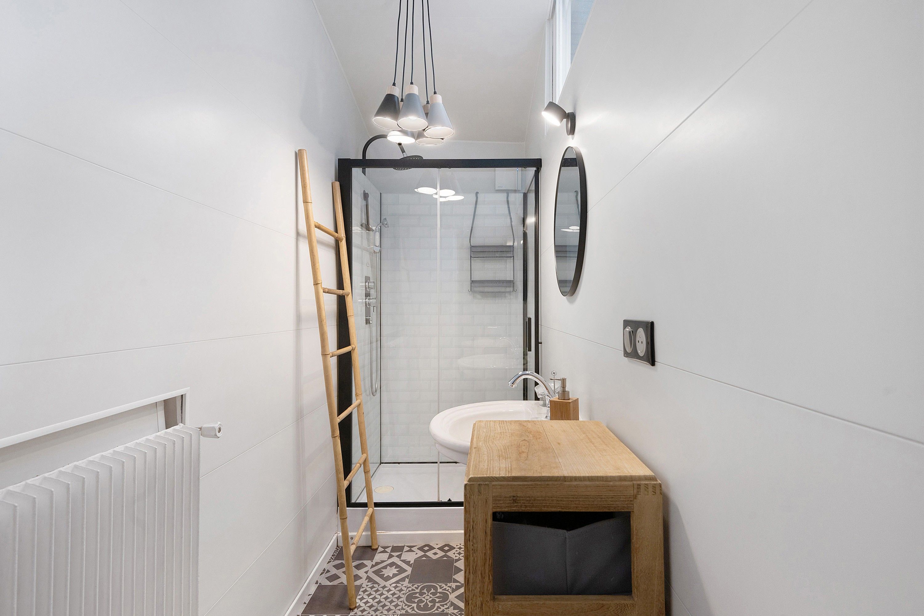 Un baño estrecho con ducha, un banco de madera y un lavamanos.