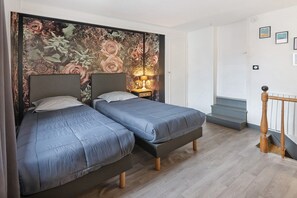 Ein Zimmer mit zwei Betten, einer Wand mit floralem Wandbild, einer Lampe und einer Treppe.