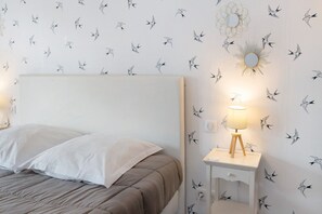 A bedroom with a bed, a bedside table with a lamp, and a wall with a bird pattern. - Au Bois Dormant Holiday Home (Crécy en Ponthieu)
