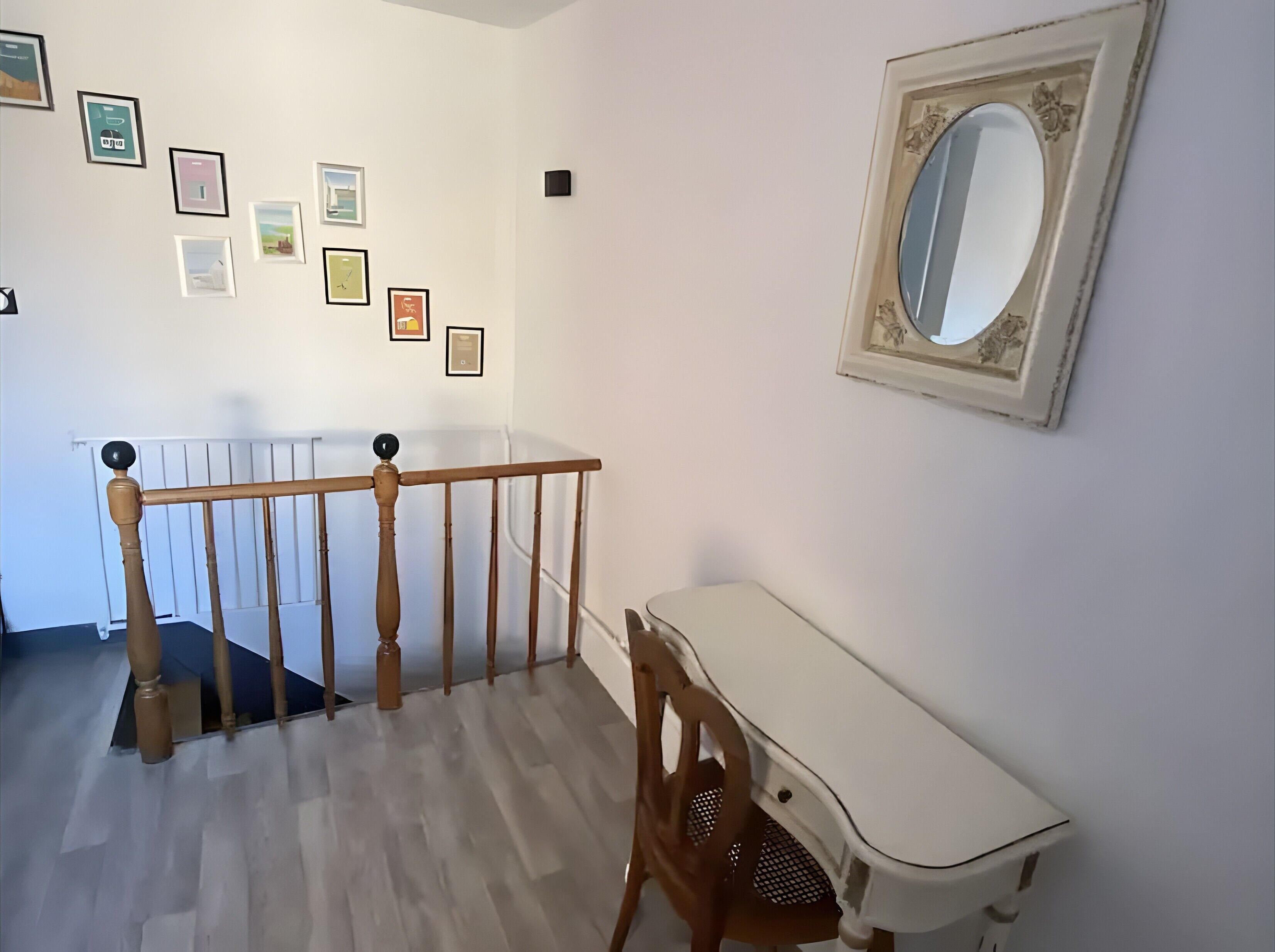 A staircase with a wooden handrail, a white desk, and a wall with framed pictures.