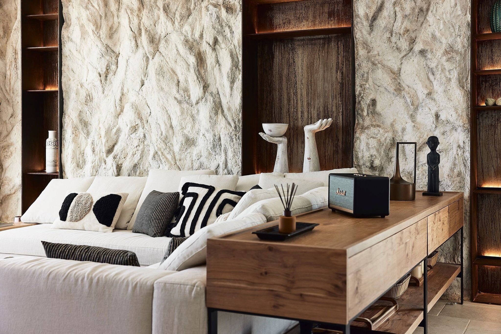 A modern bedroom with a marble wall, a wooden bedside table, a bed with patterned pillows, and a small radio.