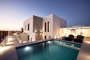 Un espace moderne aménagé au bord de la piscine, avec un mur d’accent en pierre, des sièges d’extérieur et une vue dégagée sur la piscine.