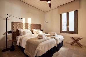 Ein Hotelzimmer mit zwei Betten, einem Holzkopfende, einer Stehlampe, einem kleinen Tisch und einem Fenster mit Jalousien.