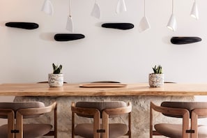 Un espace repas moderne avec une table en bois, trois chaises et des luminaires suspendus.