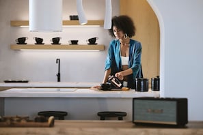 Eine moderne Küche mit einer zentralen Kochinsel, einer Kaffeemaschine und schwarzen Tassen in Regalen.