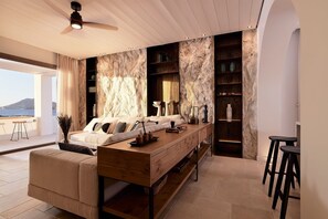 Un salon moderne avec un canapé, une table basse et des tabourets de bar. Une grande fenêtre offre une vue sur les montagnes.