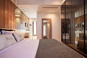 Moderni hotellihuone, jossa on suuri sänky, puinen pääty ja erillinen, peileillä varustettu vaatehuone.