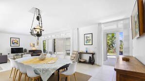 A spacious dining area with a large table, white chairs, and a chandelier. There is a television and a sofa in the adjacent living area. - Croix Du Sud (Trou d'Eau Douce)