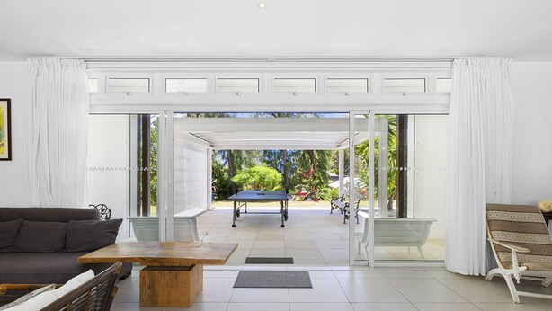 A spacious living room with a sofa, coffee table, and a view of an outdoor patio area with a table and chairs. - Croix Du Sud (Trou d'Eau Douce)