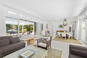 A spacious living area with a sofa, a coffee table, and a wicker chair. There is a dining table with chairs in the background. - Croix Du Sud (Trou d'Eau Douce)