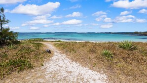 A sandy beach path leading to the ocean with clear blue water and scattered clouds. - Croix Du Sud (Trou d'Eau Douce)