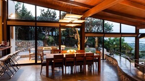 Un comedor amplio con una gran mesa de madera y sillas, ventanas grandes que ofrecen vistas al exterior, y una lámpara colgante.