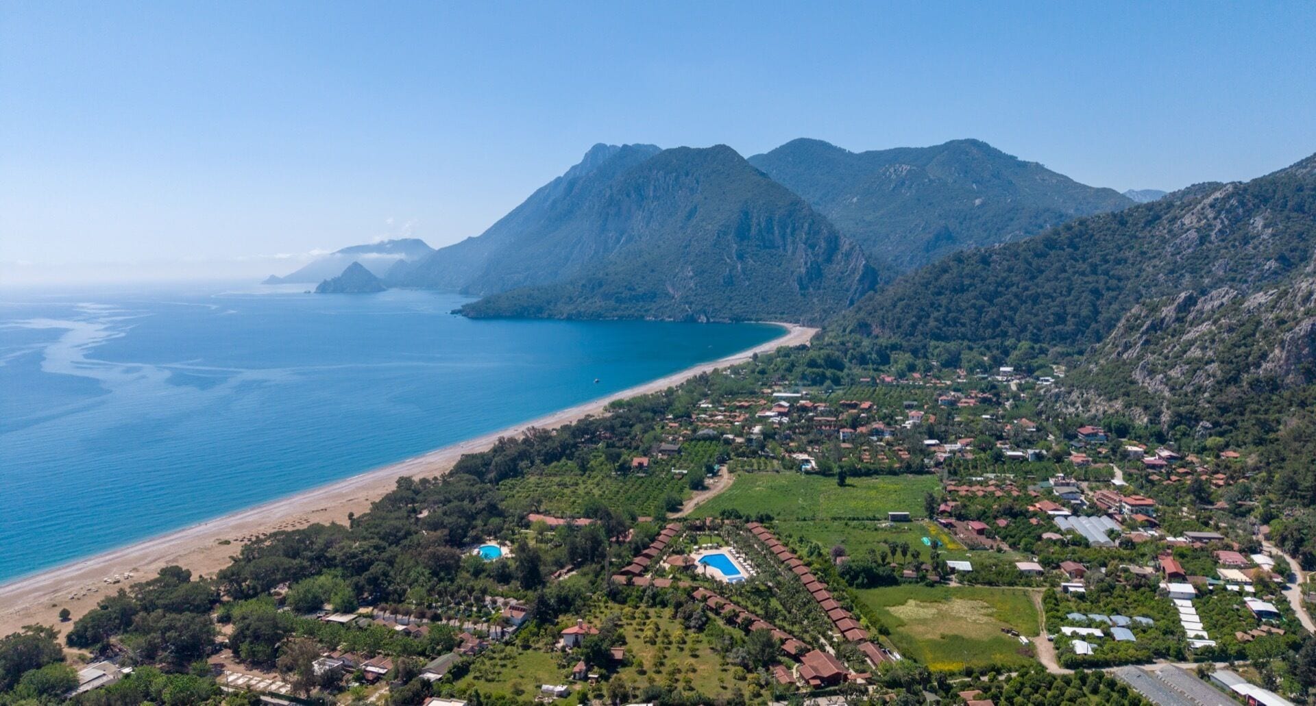 An aerial view of a coastal town with a beach, mountains, and a swimming pool complex.