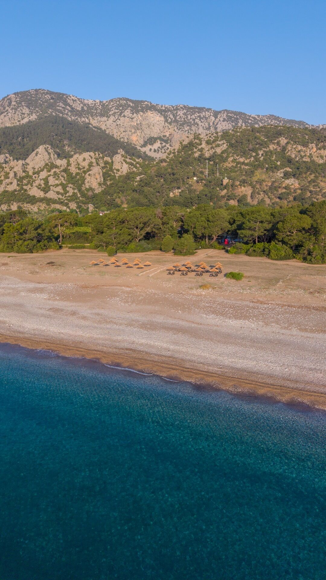 Une plage bordée d’une eau turquoise et limpide, d’un rivage rocheux et dominée par un paysage montagneux.
