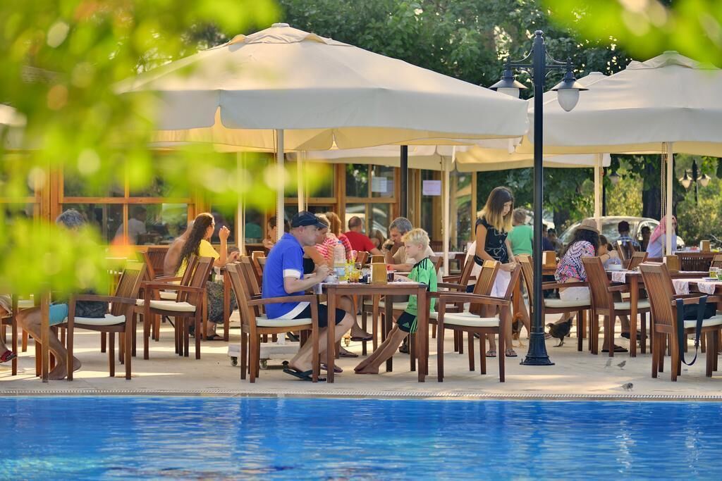 An outdoor dining area with tables and chairs, a pool, and umbrellas.
