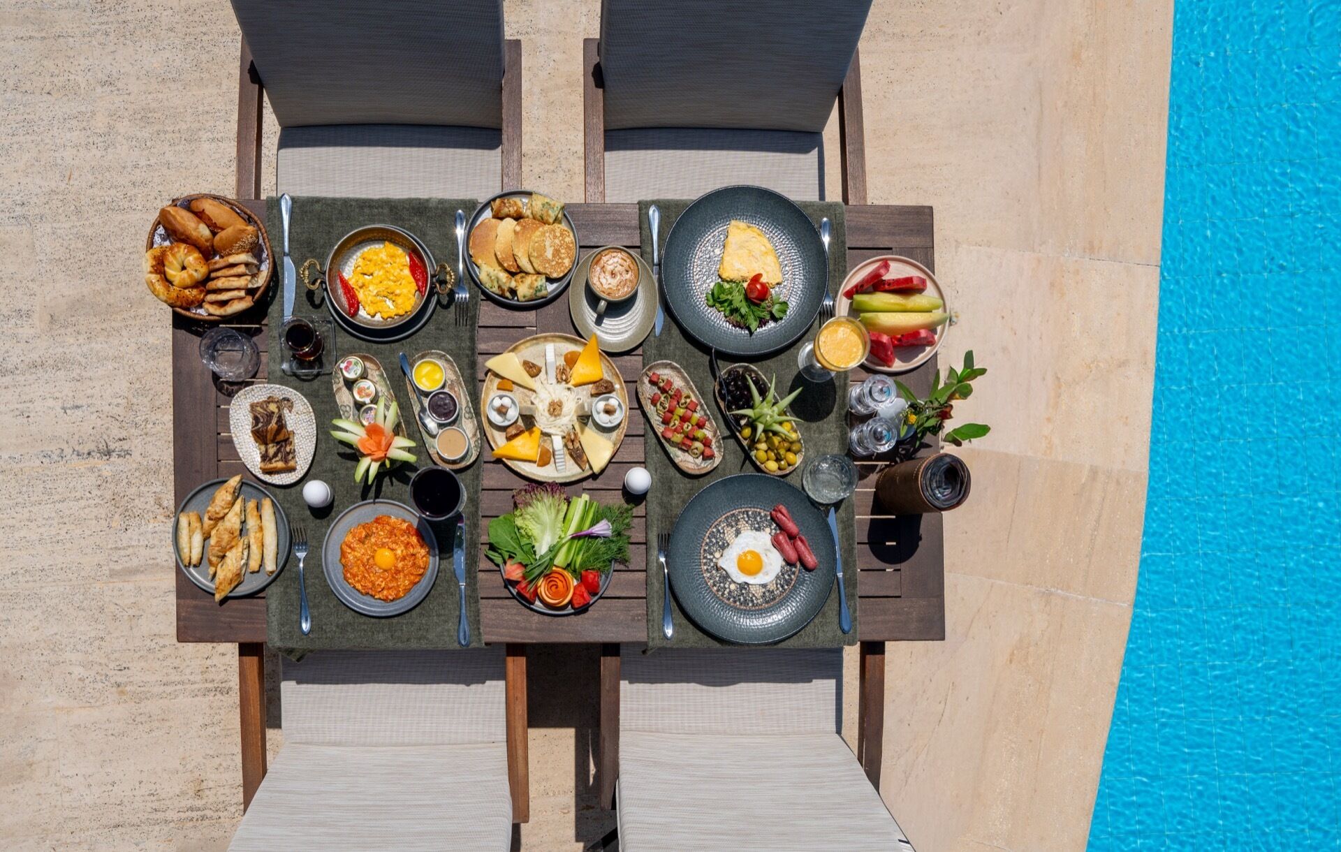 A dining table with various dishes and drinks, set against a poolside backdrop.