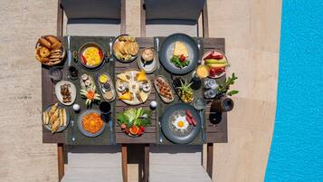 A dining table with various dishes and drinks, set against a poolside backdrop.
