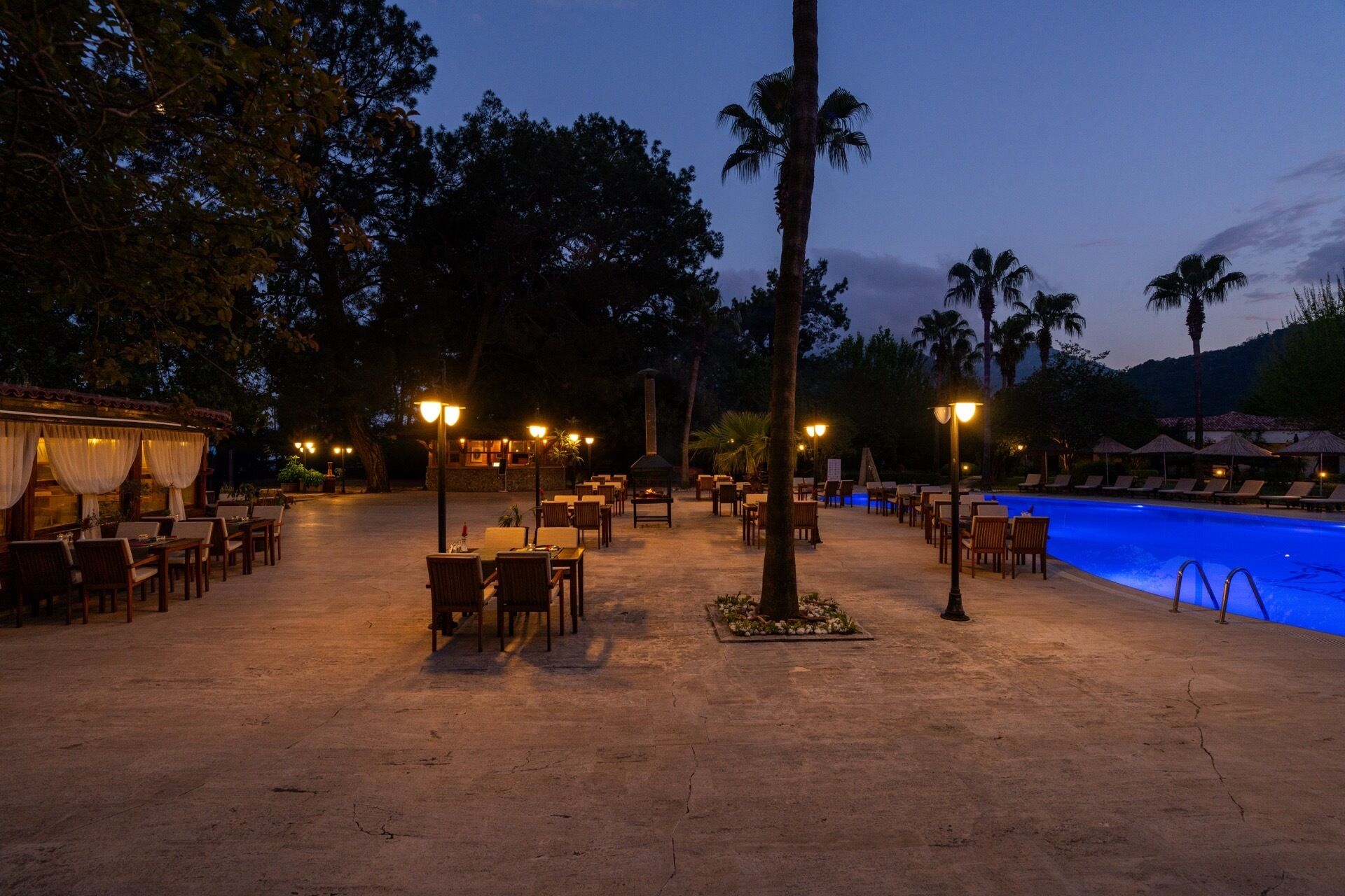 Un área de comedor al aire libre con mesas y sillas, una piscina y palmeras.