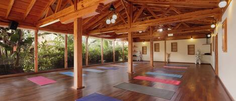 Un amplio estudio de yoga con vigas de madera y grandes ventanales con vistas a un jardín.