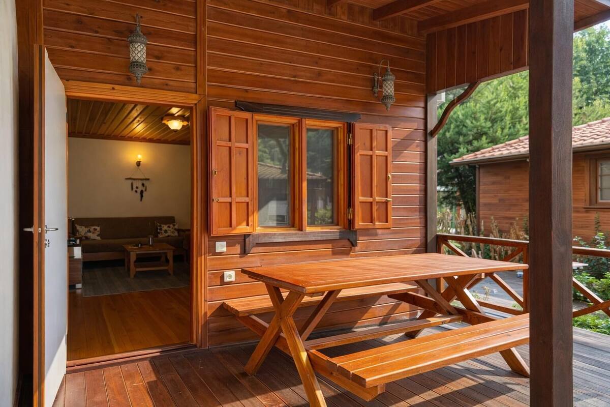 Eine Holzhütte mit einer Holzterrasse, einem Esstisch und einem gemütlichen Innenraum mit Sofa und Lampe.