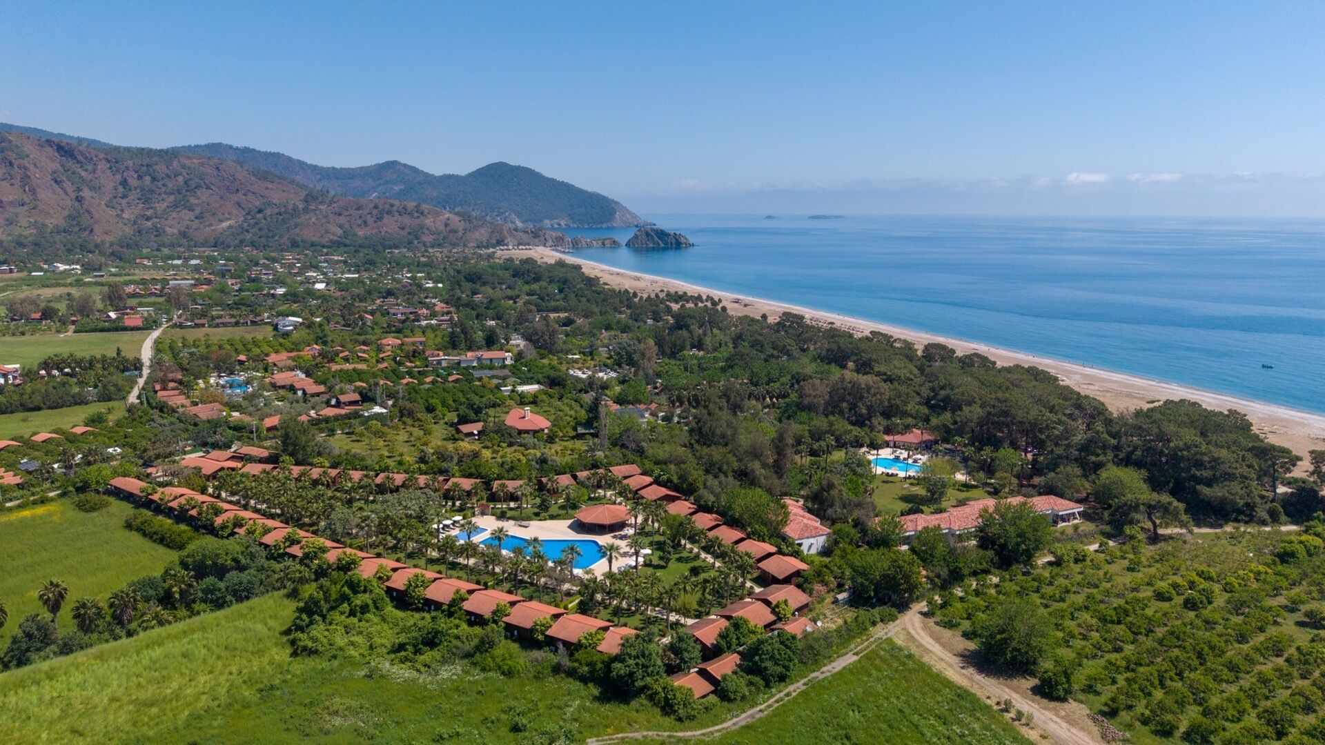 An aerial view of a coastal resort with multiple buildings, a swimming pool, and a beach.