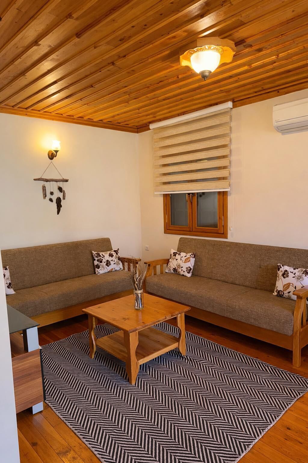 Una sala de estar acogedora con techo de madera, un conjunto de sofás, una mesa de centro y una alfombra estampada.