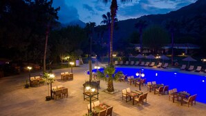 Un espace extérieur avec piscine, des chaises longues et des tables, entouré de palmiers et dominé par un paysage montagneux.