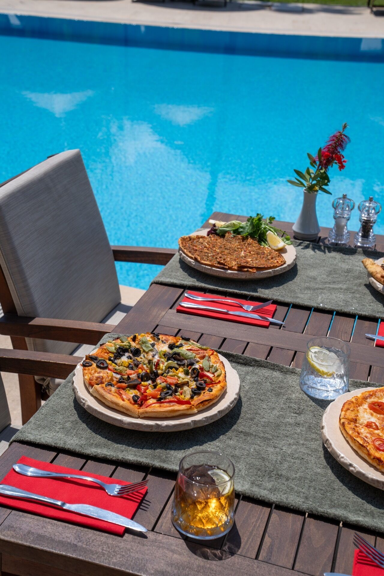 Une table à manger avec une pizza, un verre de bière et une piscine en arrière-plan.