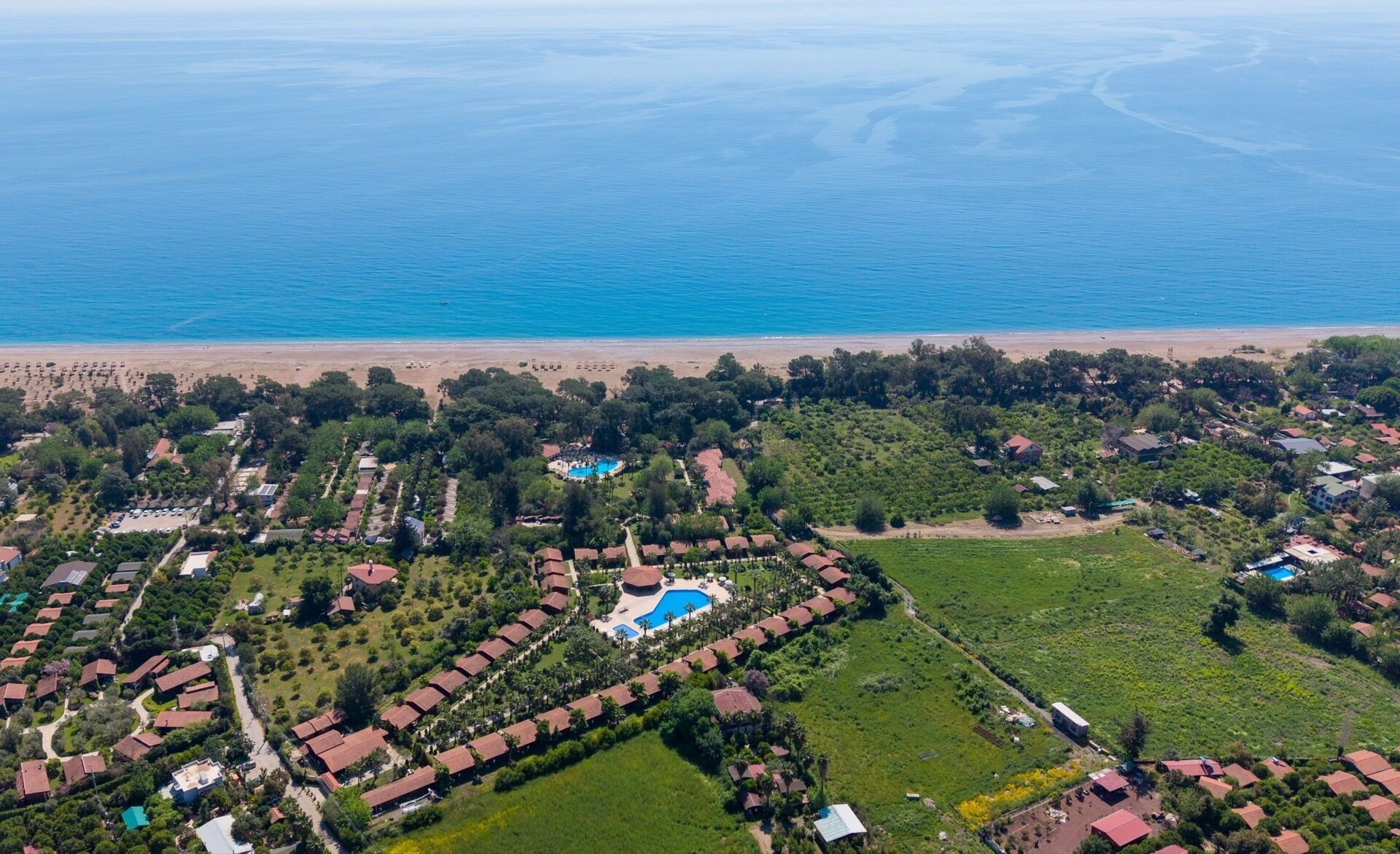 An aerial view of a coastal resort with multiple bungalow-style accommodations, a central swimming pool, and a beach.