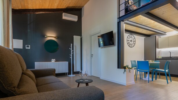 Ein modernes Wohnzimmer mit einer Couch, einem Essbereich mit blauen Stühlen, einer Küche mit Fernseher und einer Holzbalkendecke.