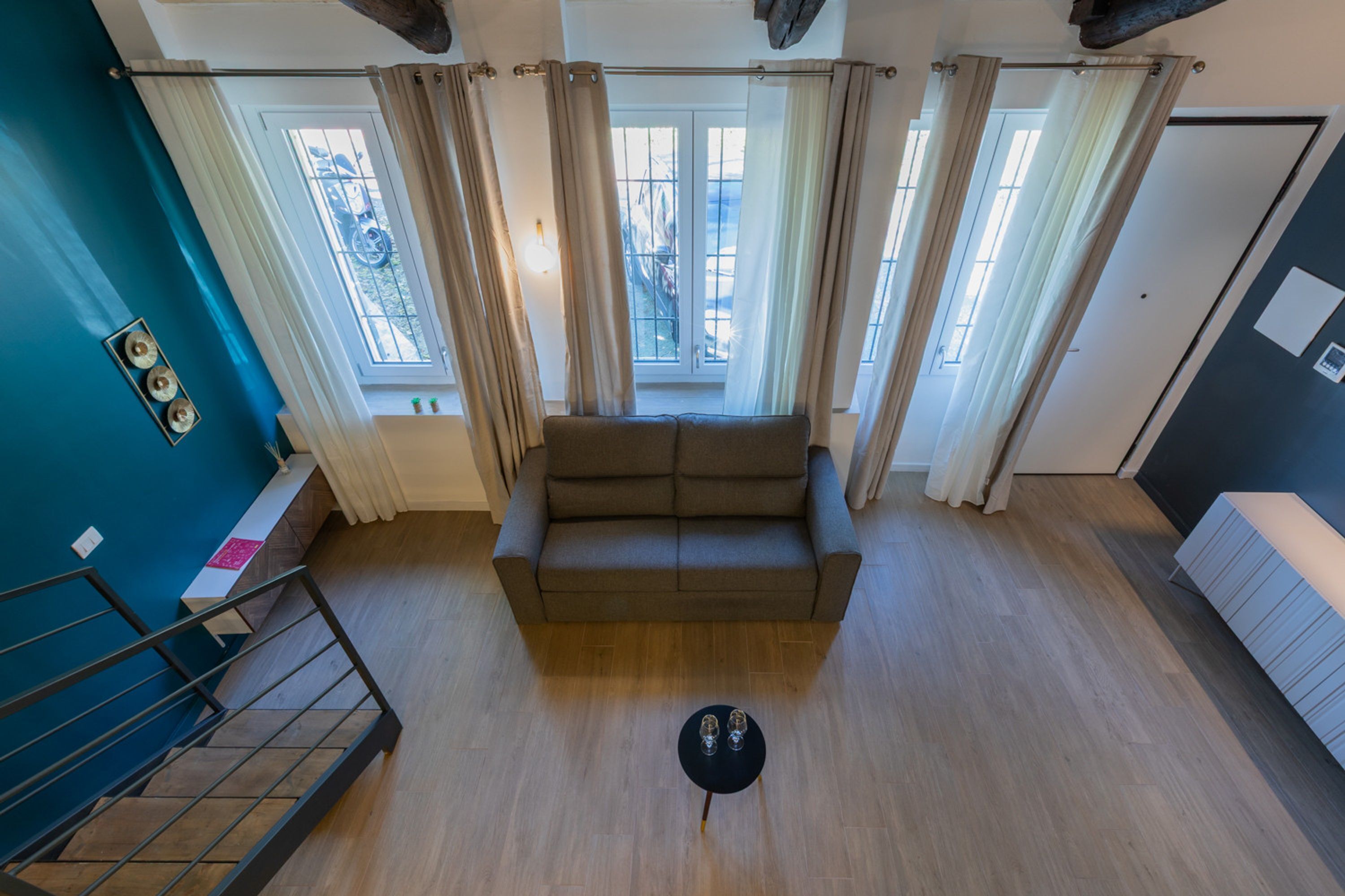 Een moderne woonkamer met een bank, een kleine tafel met glazen en een uitzicht door een raam met gordijnen.