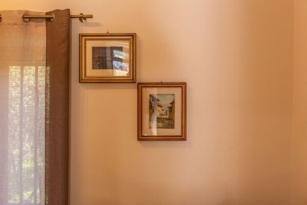 Una habitación con cortina, dos cuadros en la pared y una ventana con luz natural.