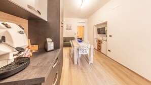Eine kleine Küche mit Kaffeemaschine, Toaster und einer Schüssel mit Brot. Ein Essbereich mit Tisch und Stühlen sowie ein an der Wand befestigter Fernseher.