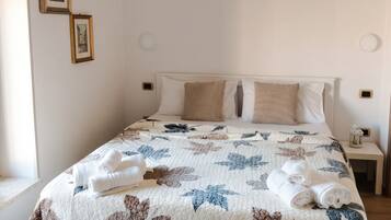 Een net opgemaakt bed met een bloemenquilt, witte kussens en opgerolde handdoeken.