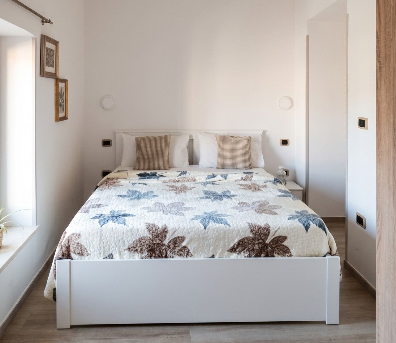 A bed with a floral bedspread, a bedside table, and a wall-mounted light fixture.
