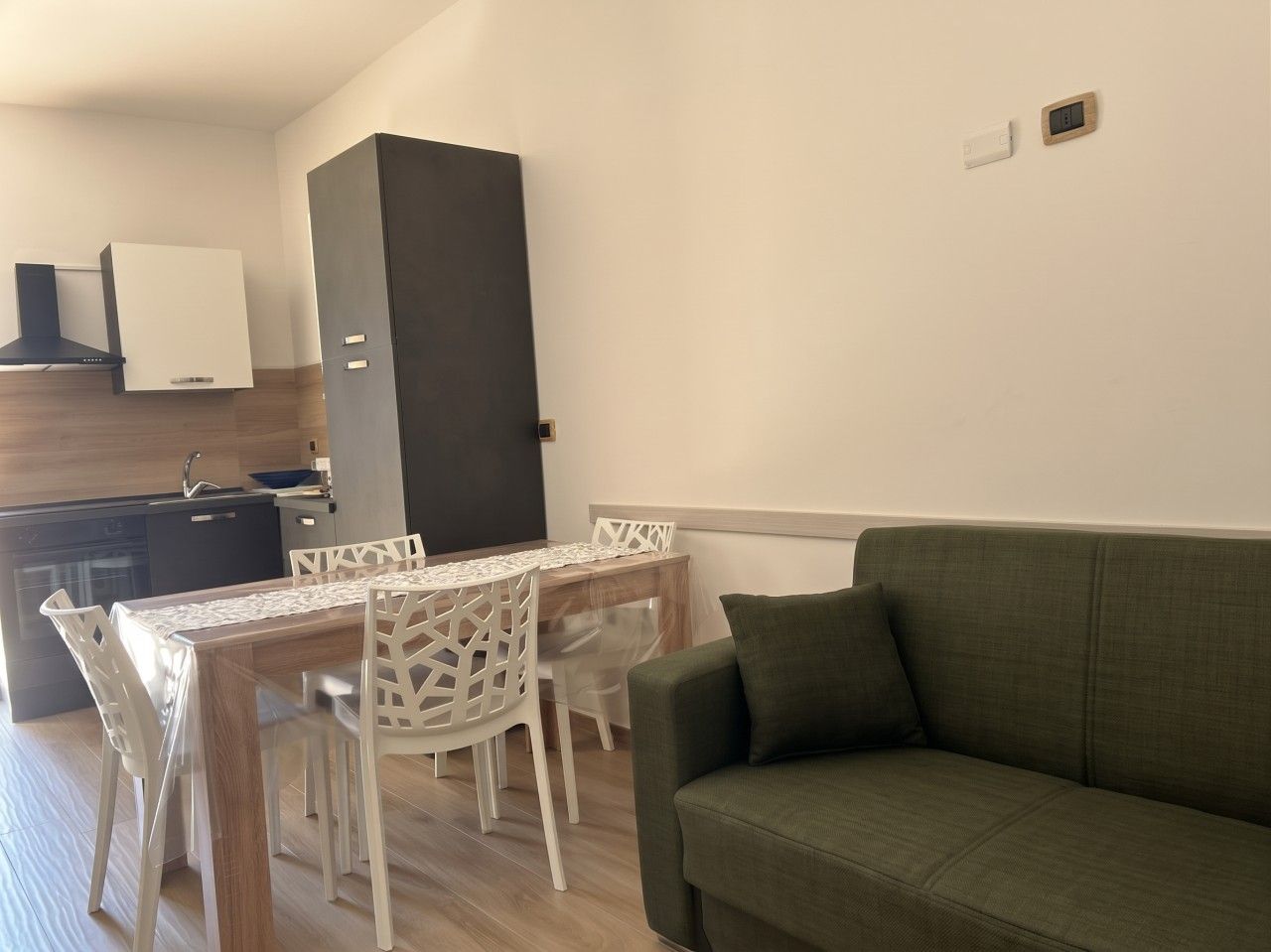 Un espace de vie compact comprenant un coin repas, une kitchenette et un canapé vert.