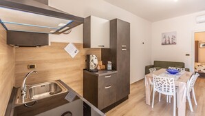 Eine kleine Küchenzeile mit Spüle, Kaffeemaschine und Schrank. Ein Essbereich mit Tisch und Stühlen ist vorhanden.