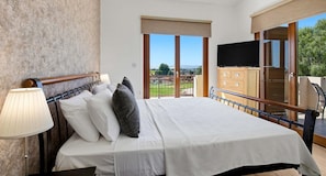 Een hotelkamer met een bed, een televisie, een houten kast en een balkon met uitzicht.