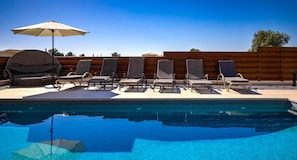 A swimming pool with lounge chairs and a sun umbrella.