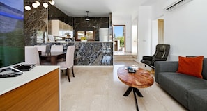 A modern living room with a grey sofa, a wooden coffee table, and a dining area with a marble backsplash.