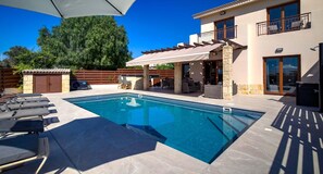 A swimming pool with lounge chairs, a covered patio area, and a stone wall.