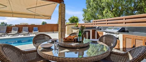 An outdoor patio with a pool, wicker furniture, a grill, and a table set for dining.