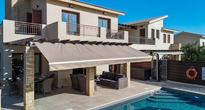 A two-story house with a covered patio area, outdoor furniture, and a swimming pool.