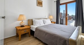 A hotel room with a bed, two bedside tables, a lamp on each table, a window with curtains, and a wall-mounted picture.