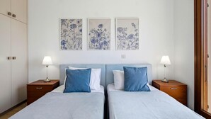 Une chambre double avec deux lits, des tables de chevet et des lampes fixées au mur.