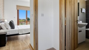 A bedroom with a bed, bedside table, and a view of a green landscape through a window.